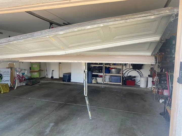 Broken garage door hanging at an angle in a garage.