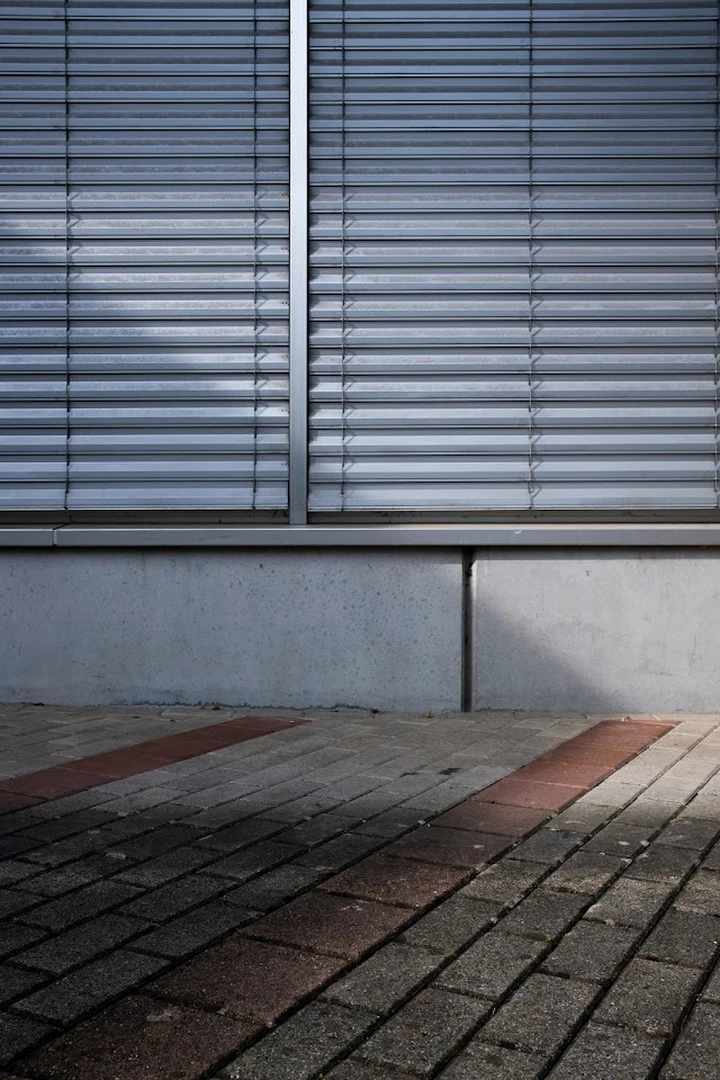 A metal facade above a concrete base and brick paving.