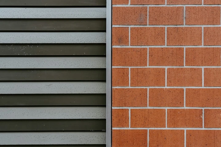 A side-by-side view of a metal shutter and a brick wall.