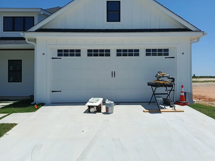 Modern white garage door with tools on a driveway.