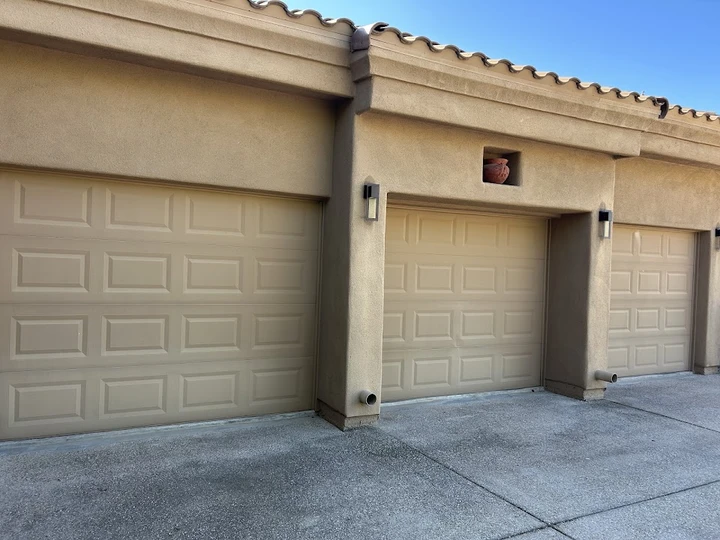 Three beige garage doors on a stucco building.
