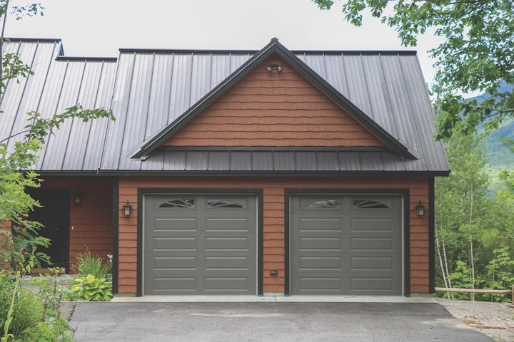 Two garage doors on a red siding home.