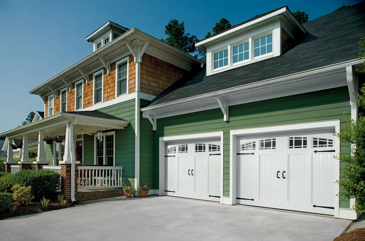 White carriage-style garage doors on a green house.