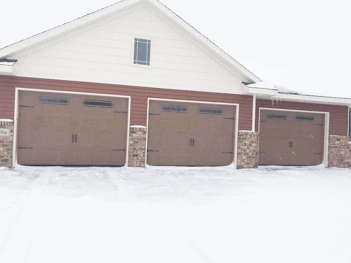 Three brown garage doors on a snowy day.
