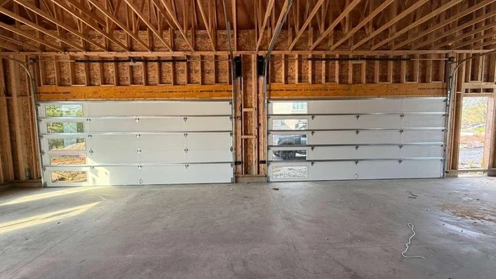 Two new garage doors installed in an unfinished garage.